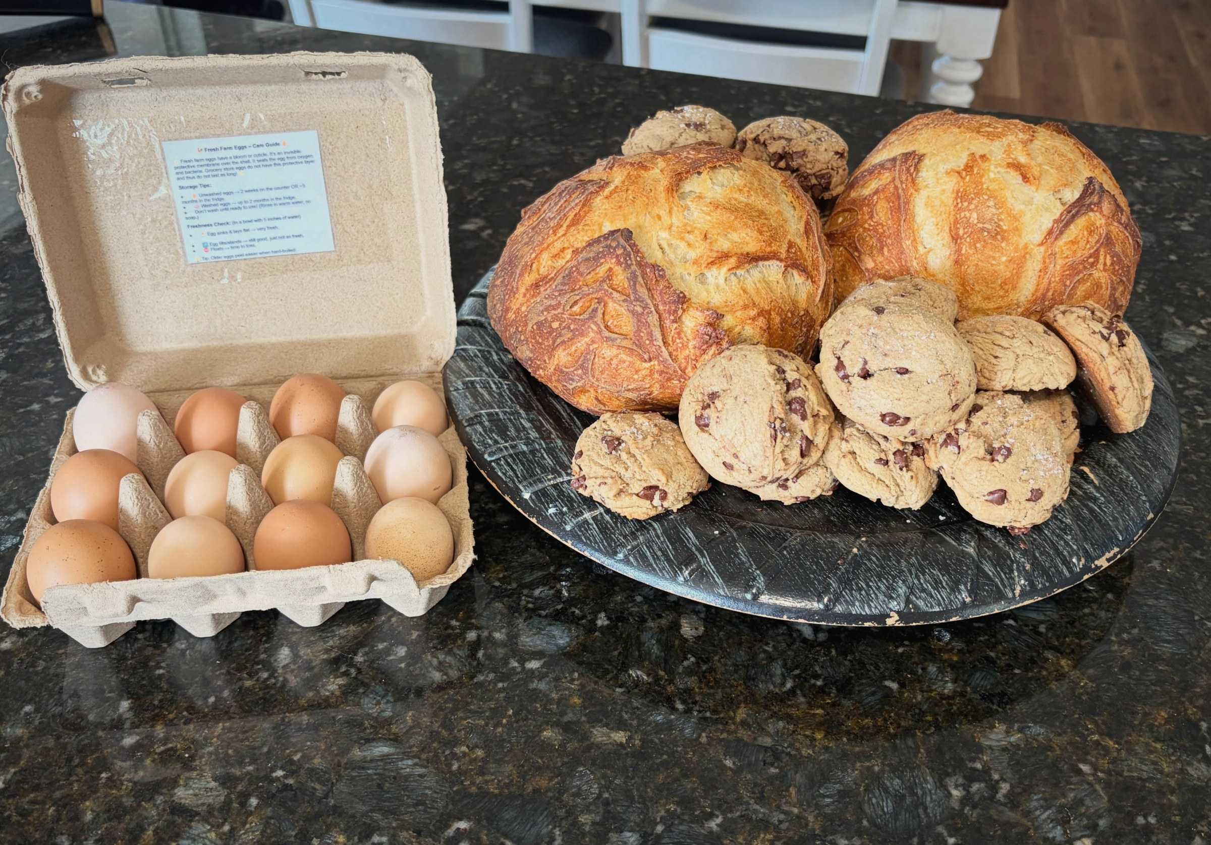 A dozen brown farm eggs beside fresh loaves and cookies